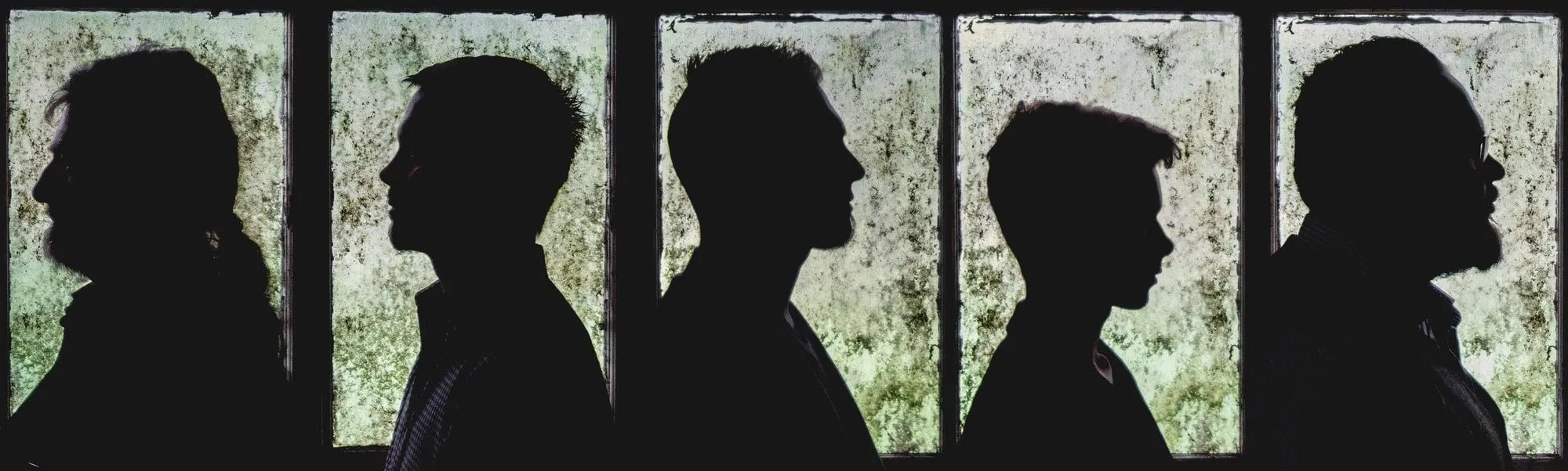 Five band members in profile silhouette against a row of weathered green windows, 2016.