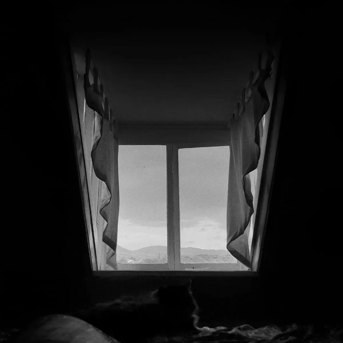 The Mourning After album cover: a black and white photo of a dark attic room looking out through a window at distant hills.